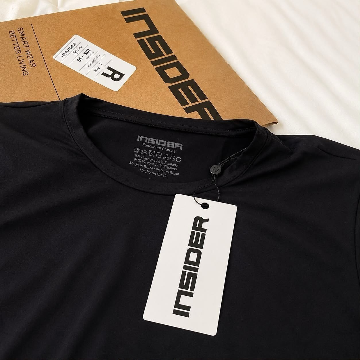 Camiseta preta da marca Insider com etiqueta de papel pendurada e embalagem de papel pardo ao fundo