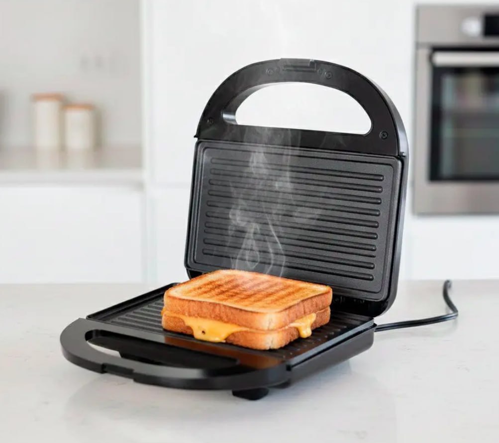 Sanduicheira Grill Itatiaia Essencial preta aberta com um sanduíche de queijo quente sendo grelhado e soltando vapor