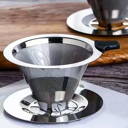 Coador de café reutilizável em aço inox com formato cônico, peneira fina, alça preta e base de apoio, apoiado sobre bandeja metálica em superfície de madeira.