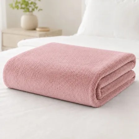 Cobertor manta soft de casal na cor rosa-claro dobrado sobre uma cama branca