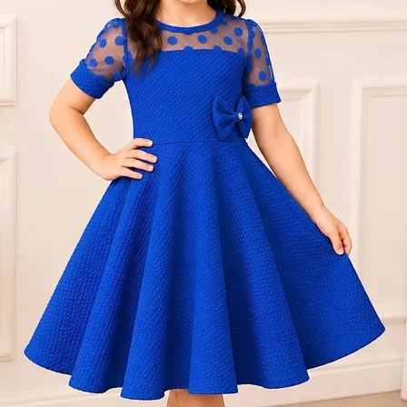 Vestido infantil azul rodado com saia ampla estilo godê, mangas curtas, decote em tule com bolinhas e laço decorativo na cintura, usado por menina em ambiente interno.