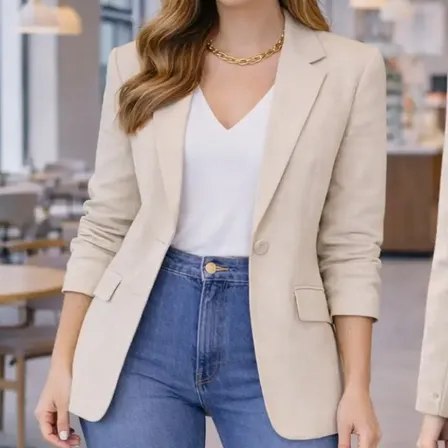 Blazer feminino de alfaiataria na cor bege com fechamento por um botão, usado sobre blusa branca e calça jeans.